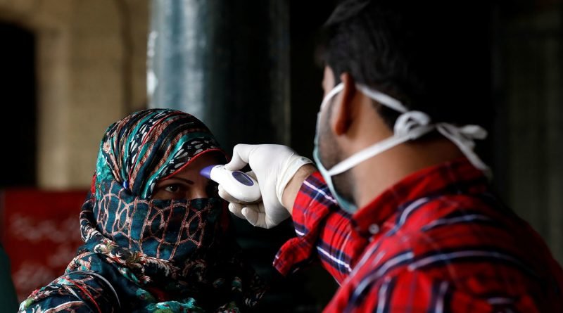 A worker checks a woman's temperature amid coronavirus fears, at the Cantonment railway station in Karachi